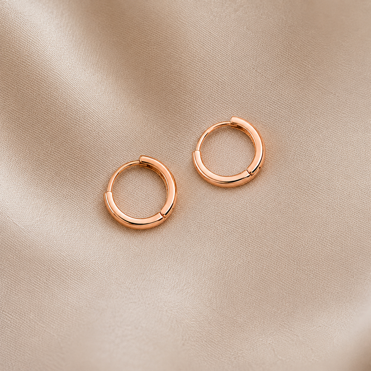 Rose gold hoop earrings on a beige fabric background